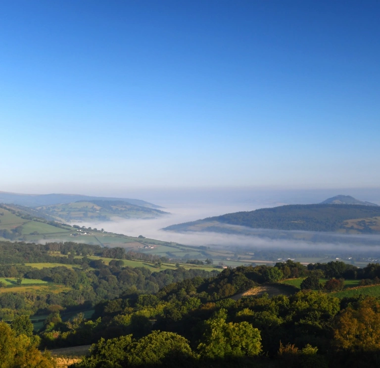 Golygfa o Fannau Brycheiniog o Llangyndir, gyda niwl yn ddwfn yn y cwm.