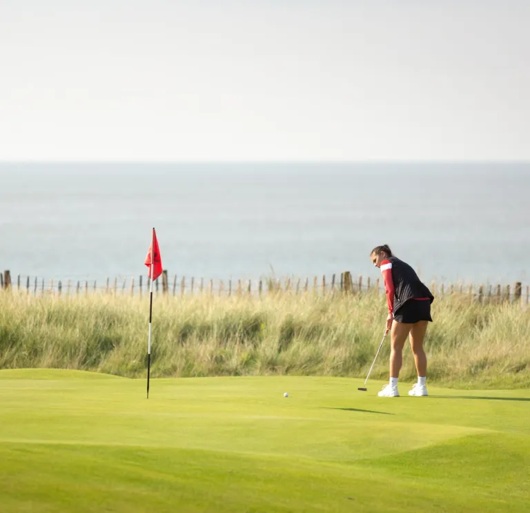Menyw yn chwarae golff yn y Royal Porthcawl, De Cymru