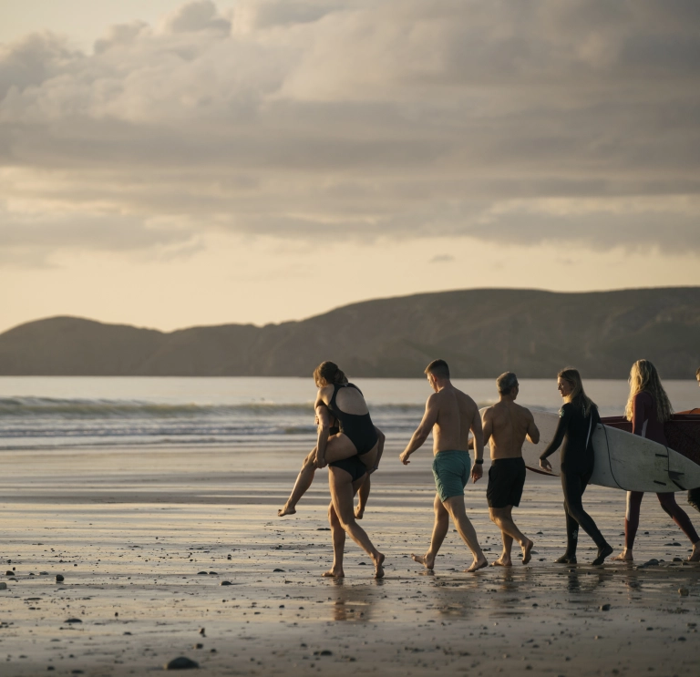 Grŵp o ffrindiau yn gwneud ioga, yn mwynhau sawna a nofio mewn dŵr oer ar draeth Niwgwl, Sir Benfro.