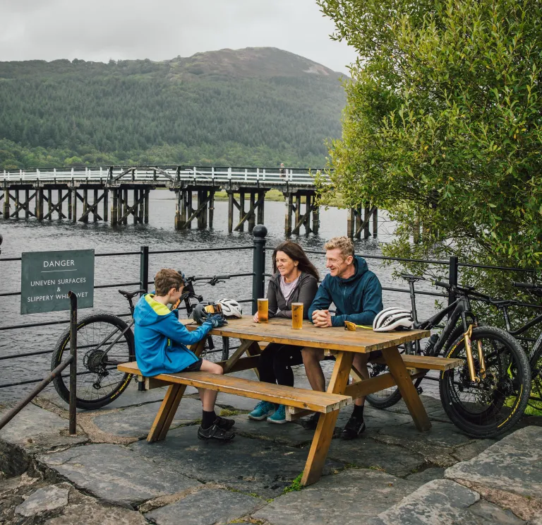 Teulu gyda beiciau yn eistedd wrth fainc bicnic, Llwybr Mawddach