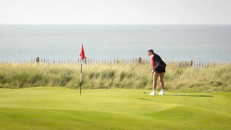 Menyw yn chwarae golff yn y Royal Porthcawl, De Cymru