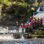 Grŵp o bobl yn deifio mewn dillad diogelwch yn agos i rhaeadr.